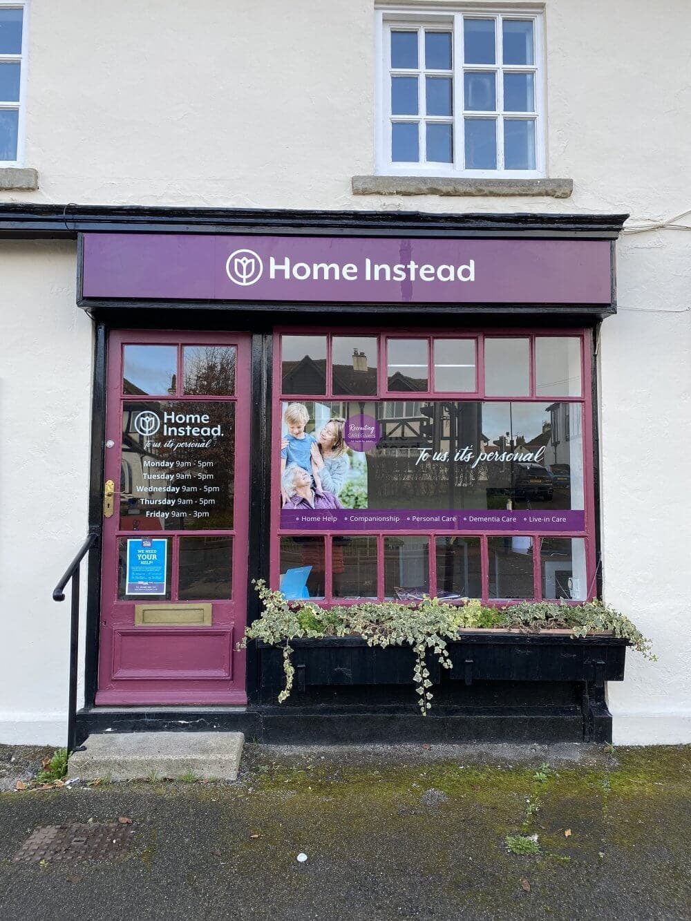 Front view of "Home Instead" office with purple signage and window display showing services and business hours. - Home Instead