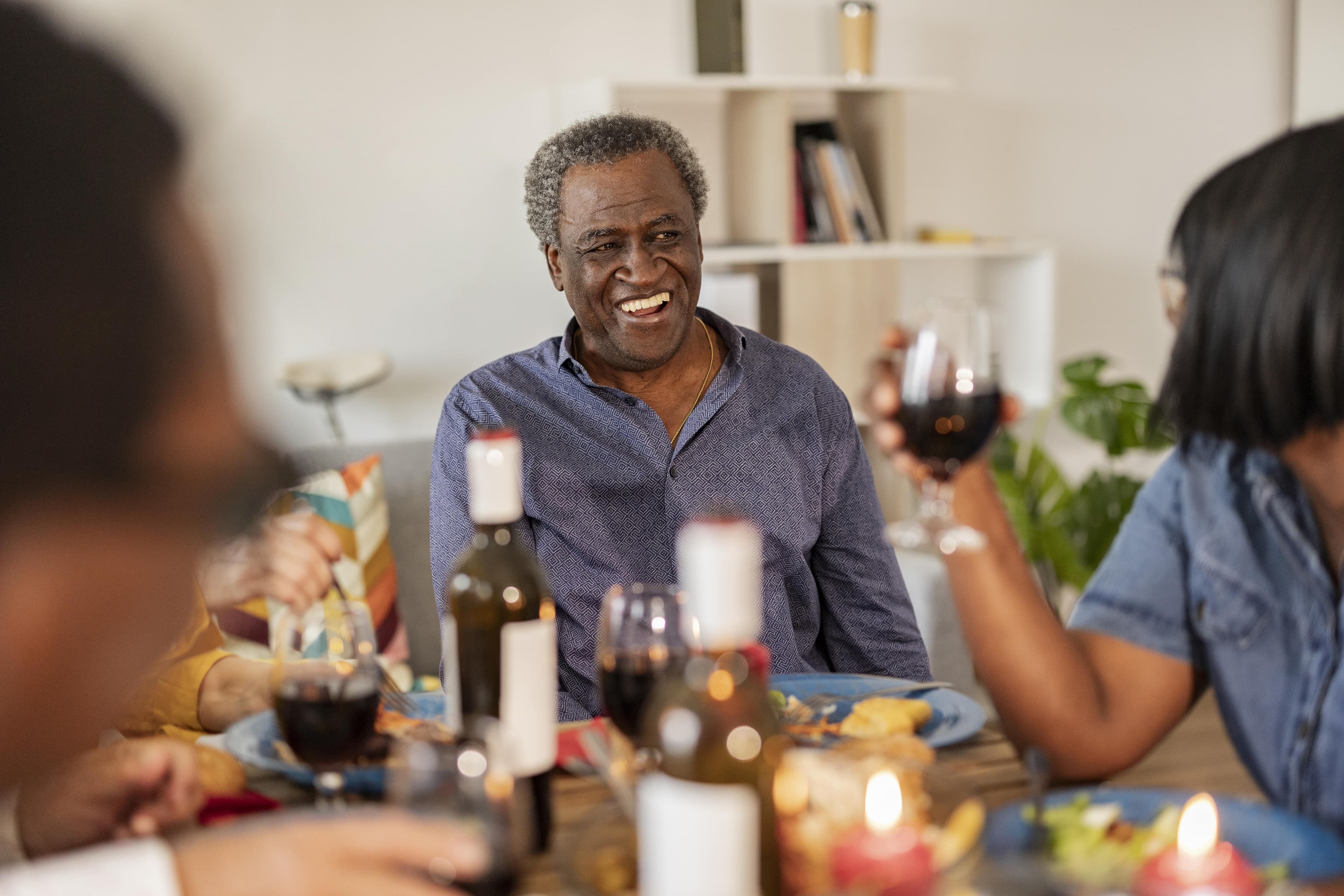 Smiling man enjoying a meal and drinks with friends at a warmly lit dinner table. - Home Instead