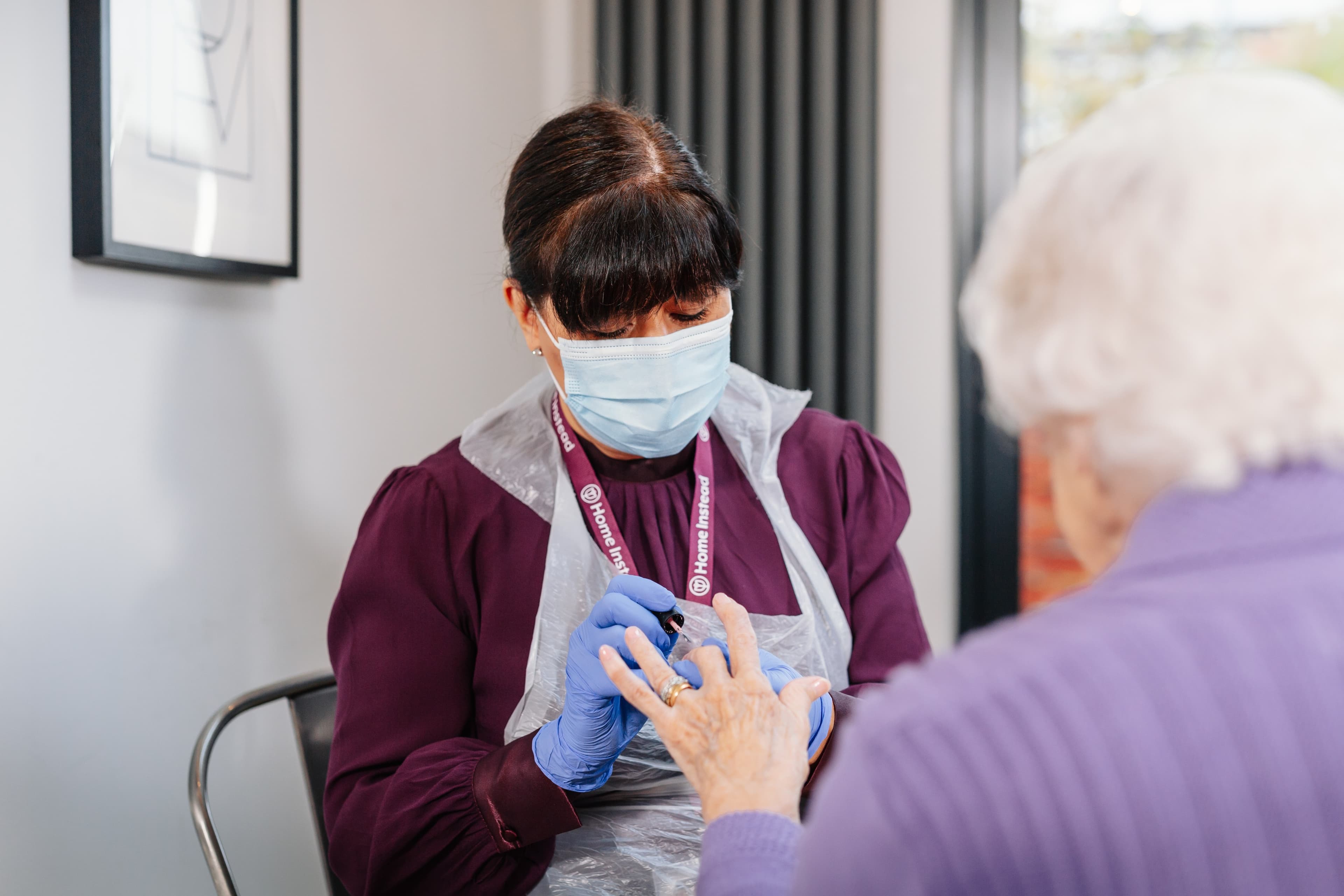 Healthcare worker wearing a mask and gloves cares for an elderly person's hand in a medical setting. - Home Instead