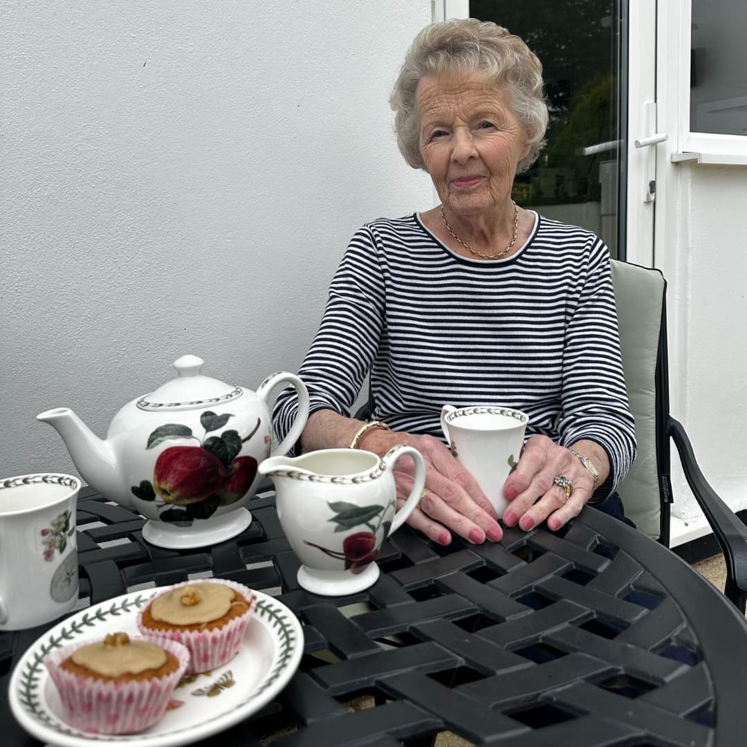 An elderly woman sitting outside having tea and cake