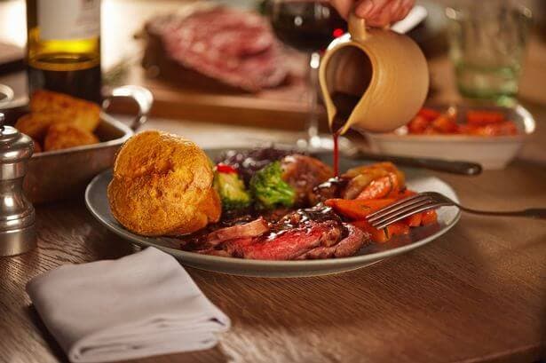 A plate of roast beef with vegetables and Yorkshire pudding, with gravy being poured from a jug. - Home Instead