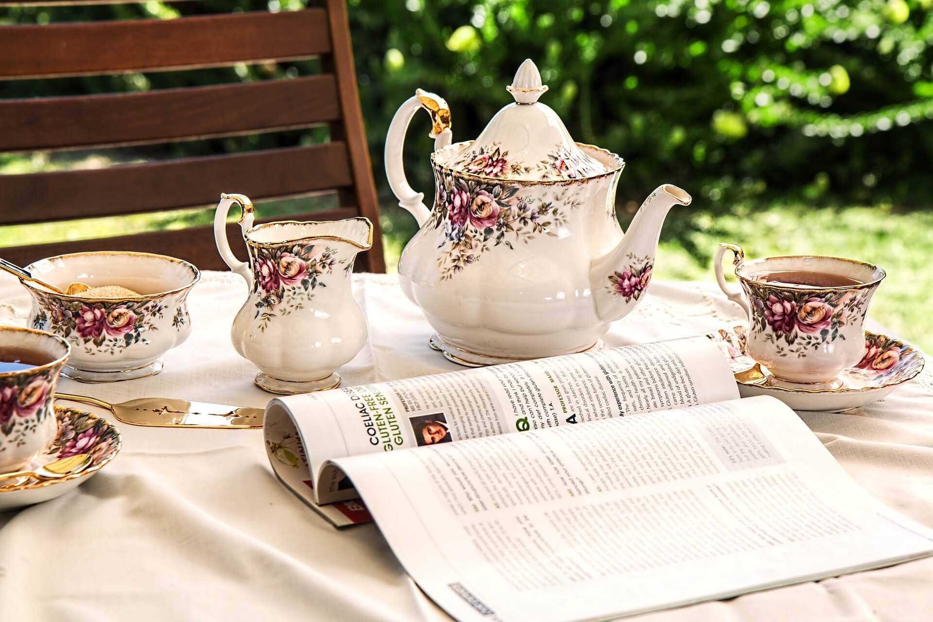 A floral porcelain tea set on a table with an open book in an outdoor garden setting. - Home Instead