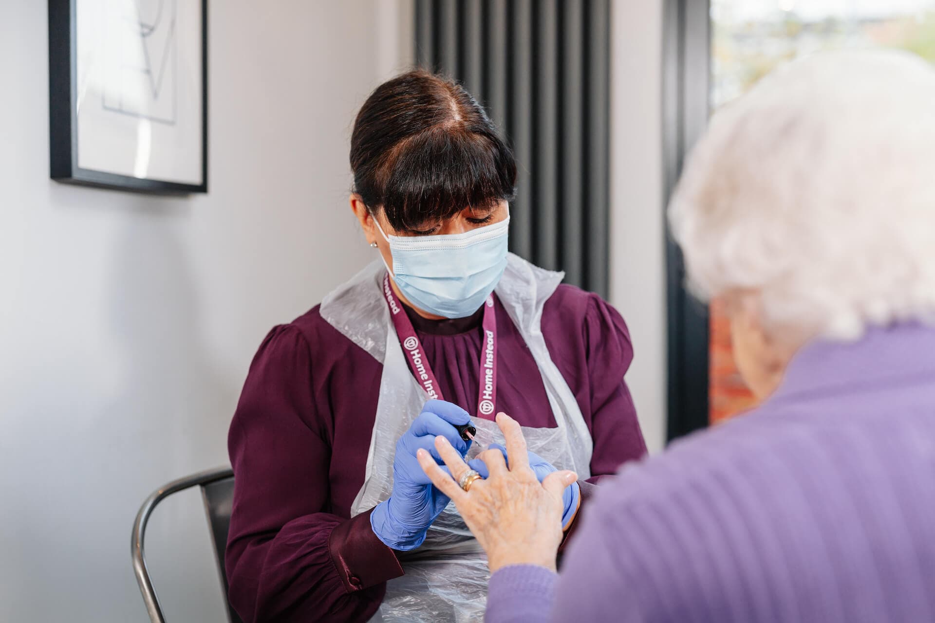A healthcare worker in protective gear tends to an elderly person’s hand in a clinical setting. - Home Instead
