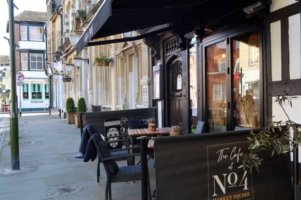 Outdoor café with seating and black signage that reads "The Café at No. 4 Market Square" on a quiet, historic street. - Home Instead