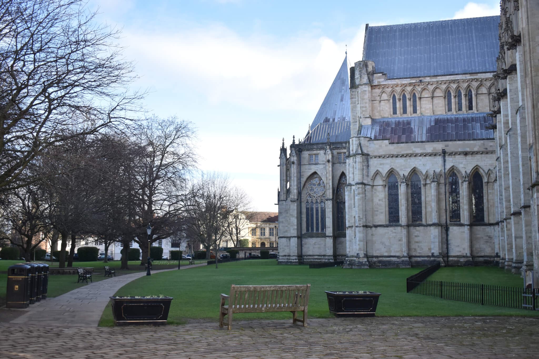A peaceful scene of a cathedral with benches and trees on a cloudy day, with a clear view of the cathedral's architecture. - Home Instead