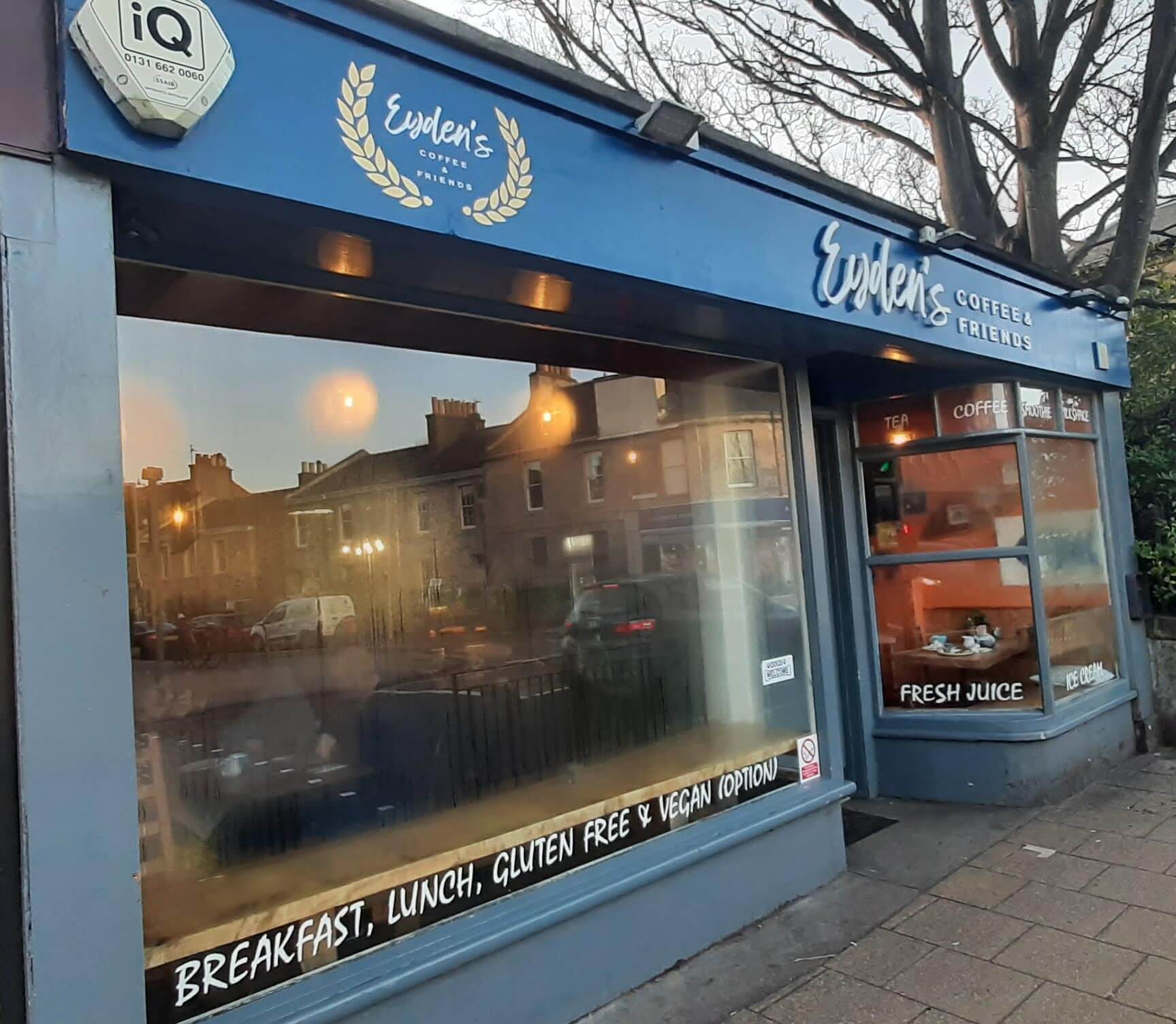 Exterior of a blue coffee shop with a sign reading "Evelen's Coffee & Friends," advertising breakfast, lunch, and vegan options. - Home Instead