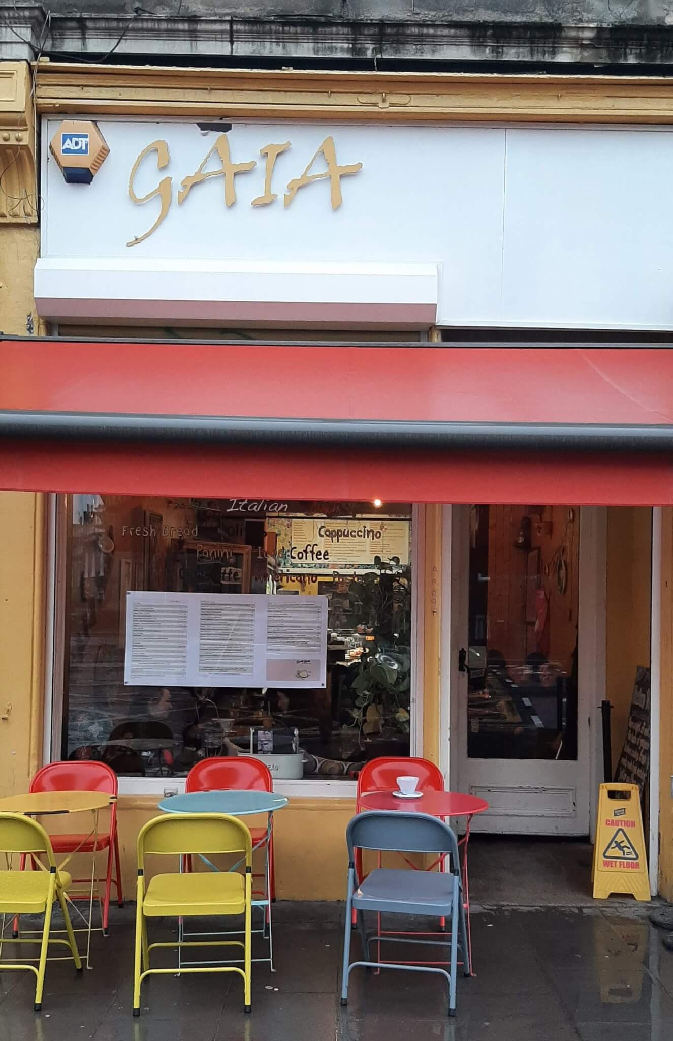 A small cafe with a red awning, colorful chairs, and tables on the sidewalk, with the sign "GAIA" above the entrance. - Home Instead