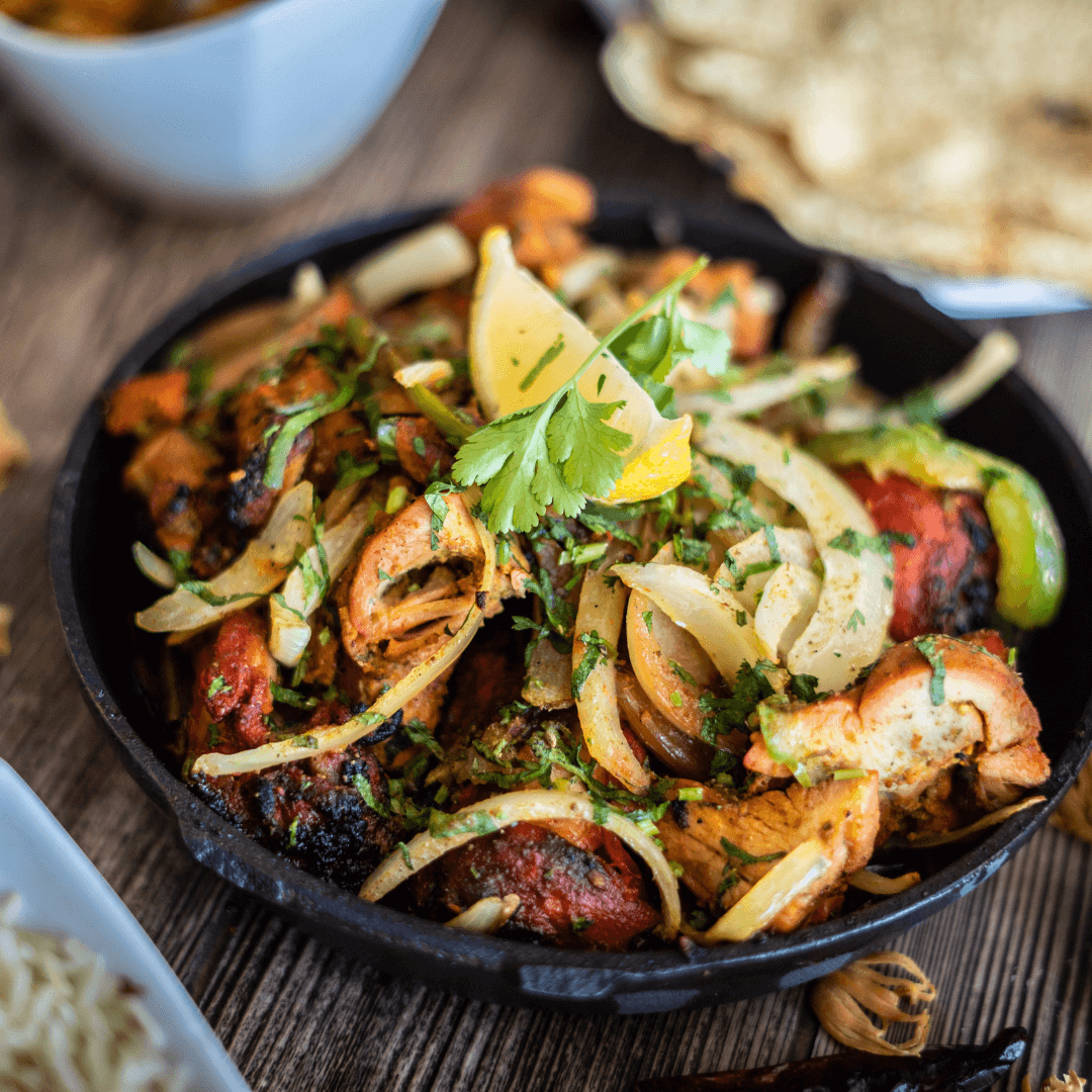 A skillet of chicken fajitas with onions and cilantro, garnished with a lemon wedge and cilantro sprig on top. - Home Instead