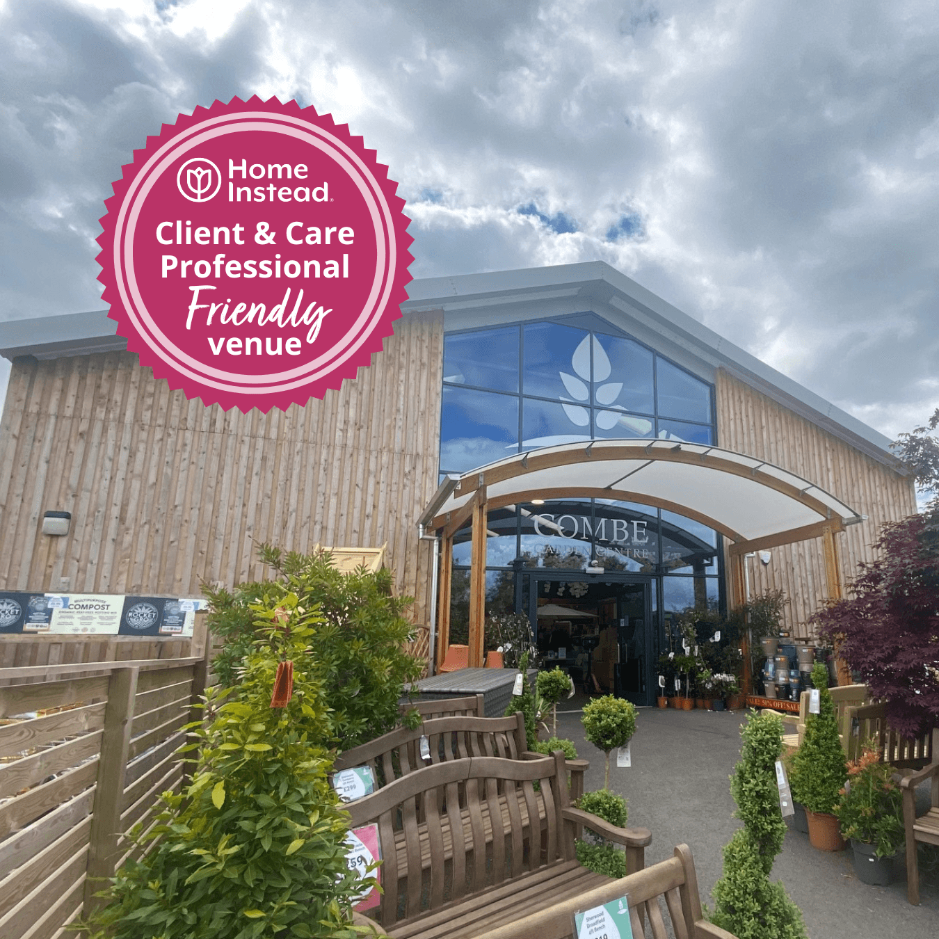 Exterior of a wooden building under a cloudy sky with a "Friendly Venue" badge on the top left side. - Home Instead