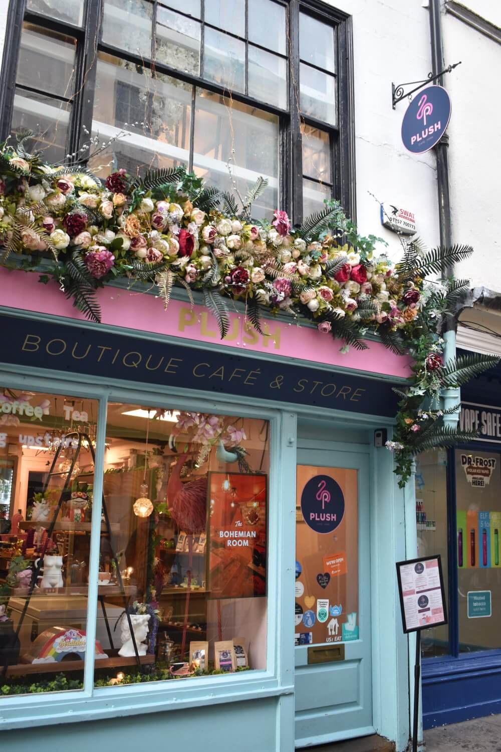 A boutique café with floral decorations on its storefront, named "Plush", in a quaint urban neighborhood. - Home Instead