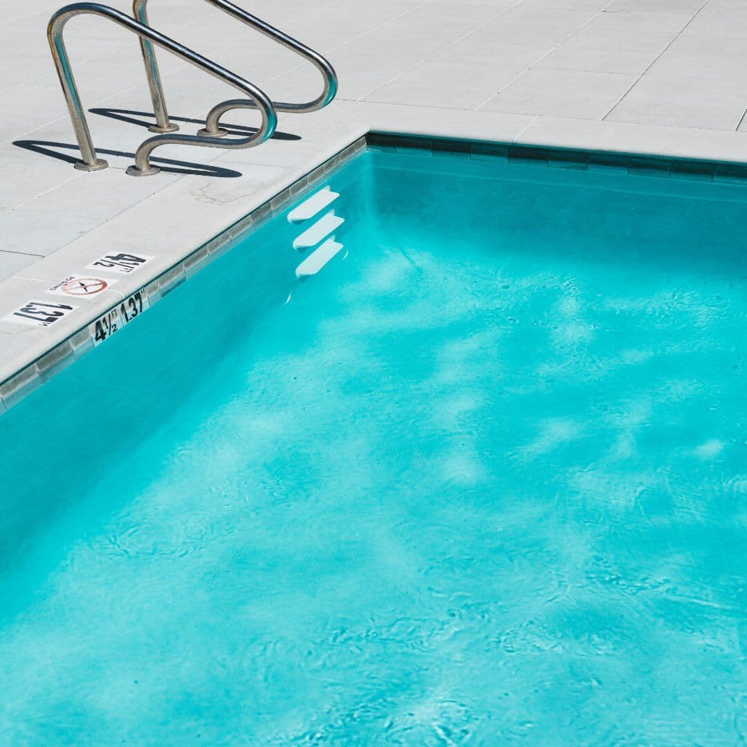 A clear swimming pool with metal handrails and depth markings on the side is shown on a sunny day. - Home Instead
