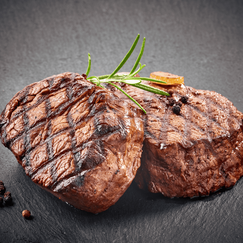 Two pieces of grilled steak garnished with rosemary, served on a slate surface. - Home Instead