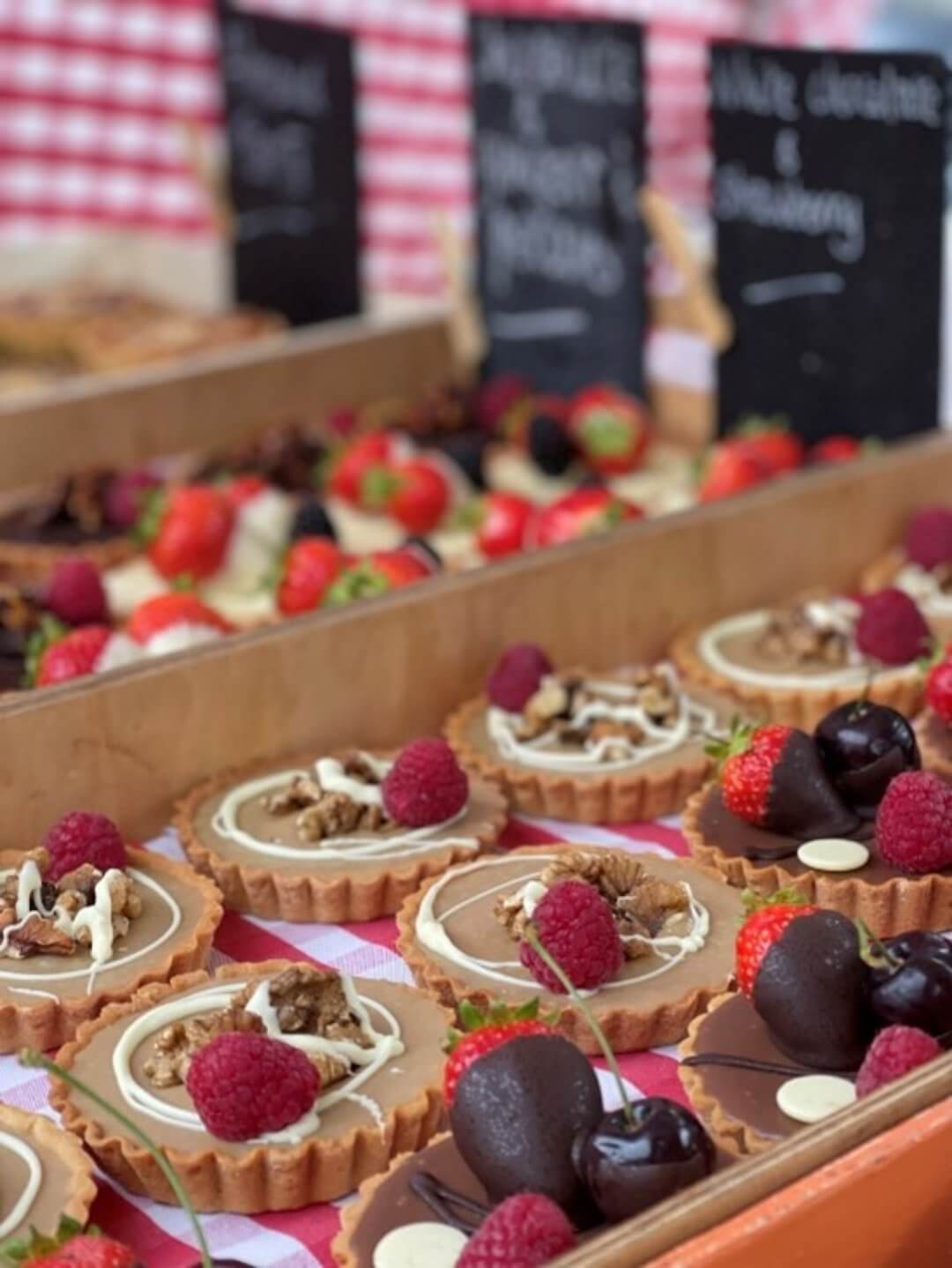 A variety of pastries topped with raspberries, strawberries, and chocolate displayed at a market stall. - Home Instead