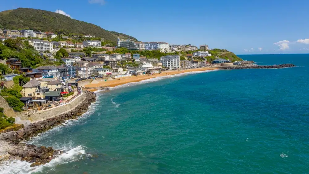 Aerial view of a coastal town with buildings, sandy beach, and turquoise waters on a bright, sunny day. - Home Instead