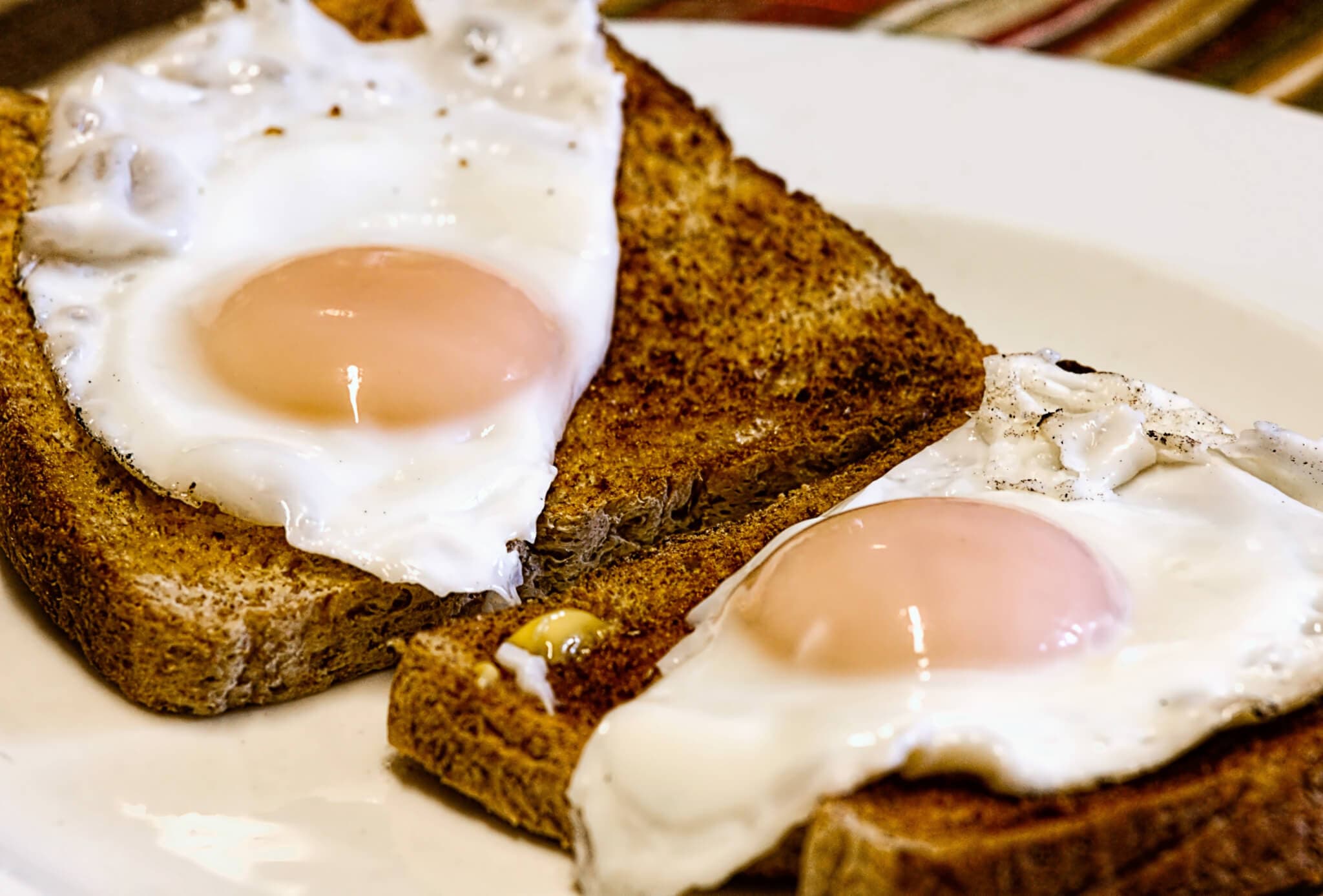 Two sunny-side-up eggs on toasted bread slices on a white plate. - Home Instead