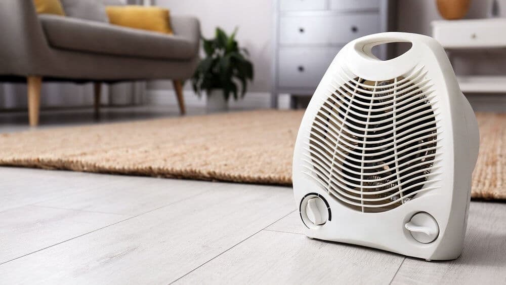Portable white heater on a wooden floor in a cozy living room with a couch and plants in the background. - Home Instead