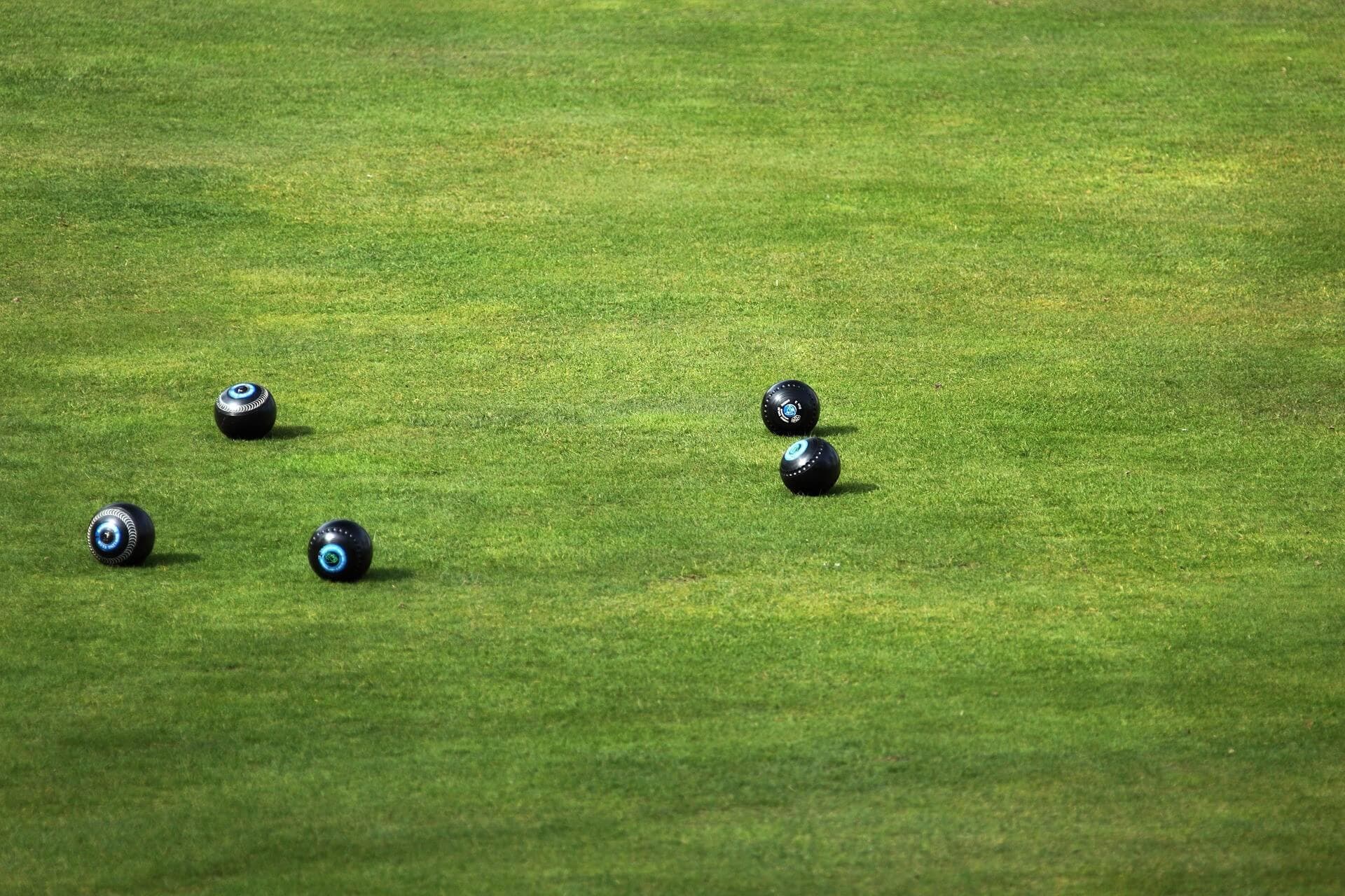 Black bowls scattered on a neatly trimmed lawn during a game of lawn bowling. - Home Instead