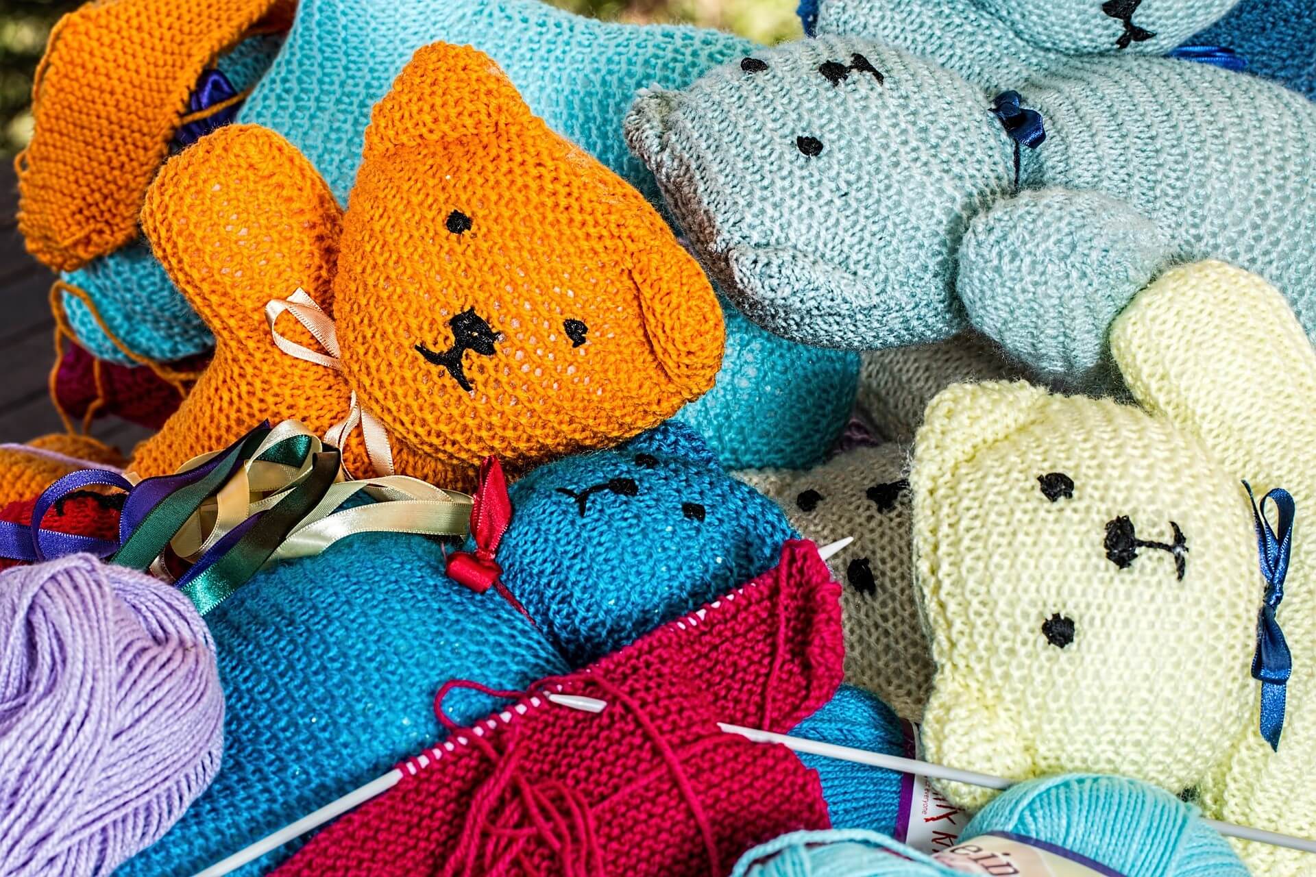 A pile of colorful knitted teddy bears surrounded by yarn balls and knitting needles. - Home Instead