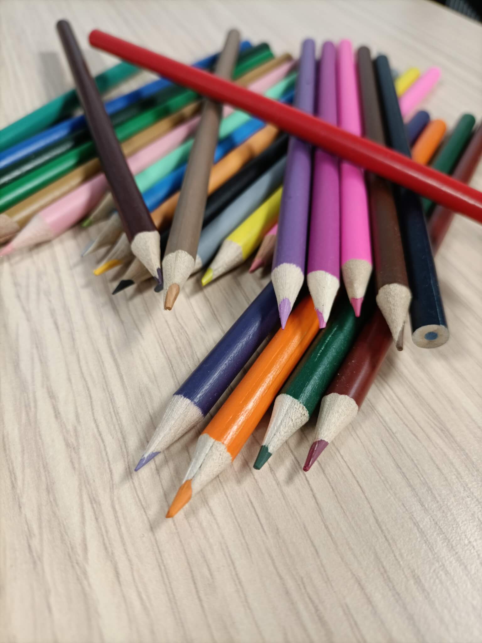 A scattered pile of colored pencils on a wooden surface, featuring various colors including red, pink, blue, and green. - Home Instead