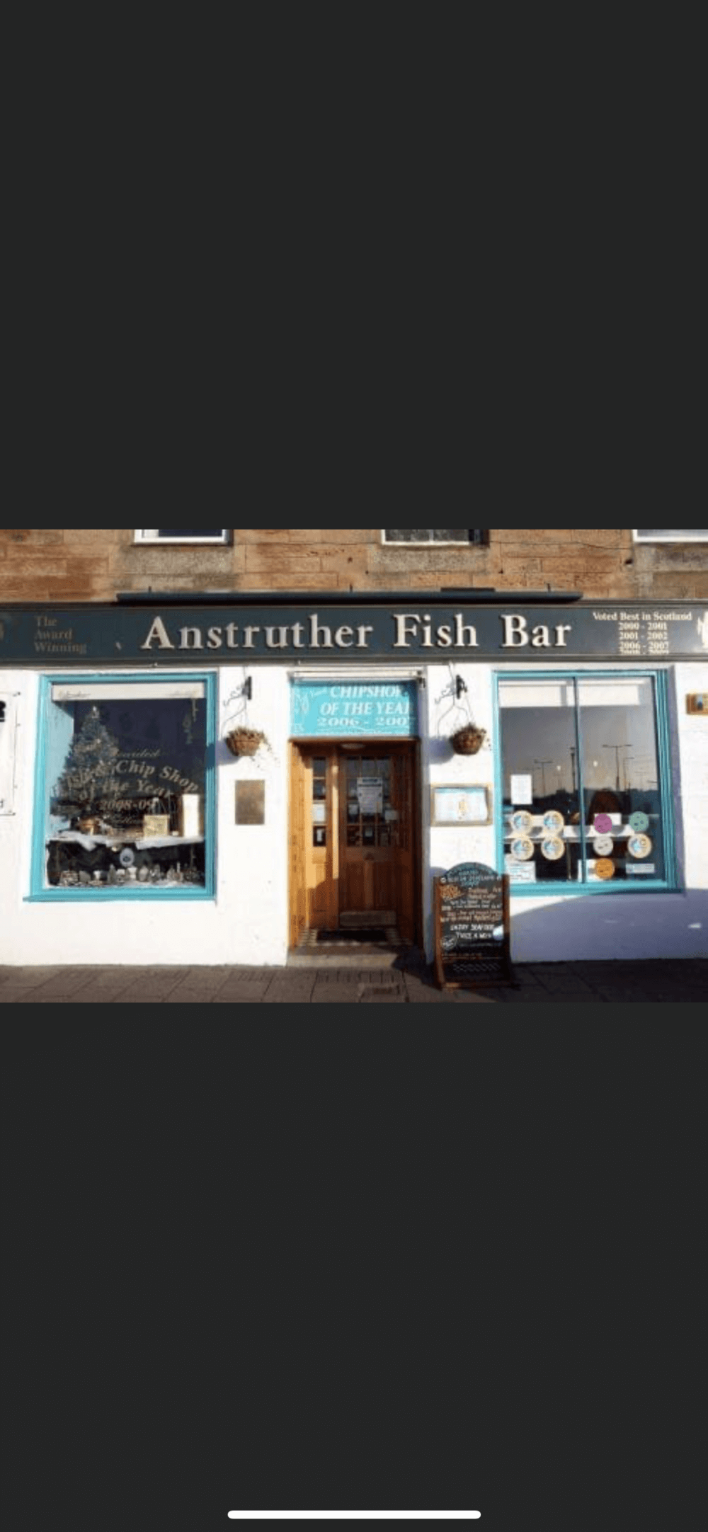 A fish and chips restaurant named "Anstruther Fish Bar" with a wooden door and blue storefront. - Home Instead