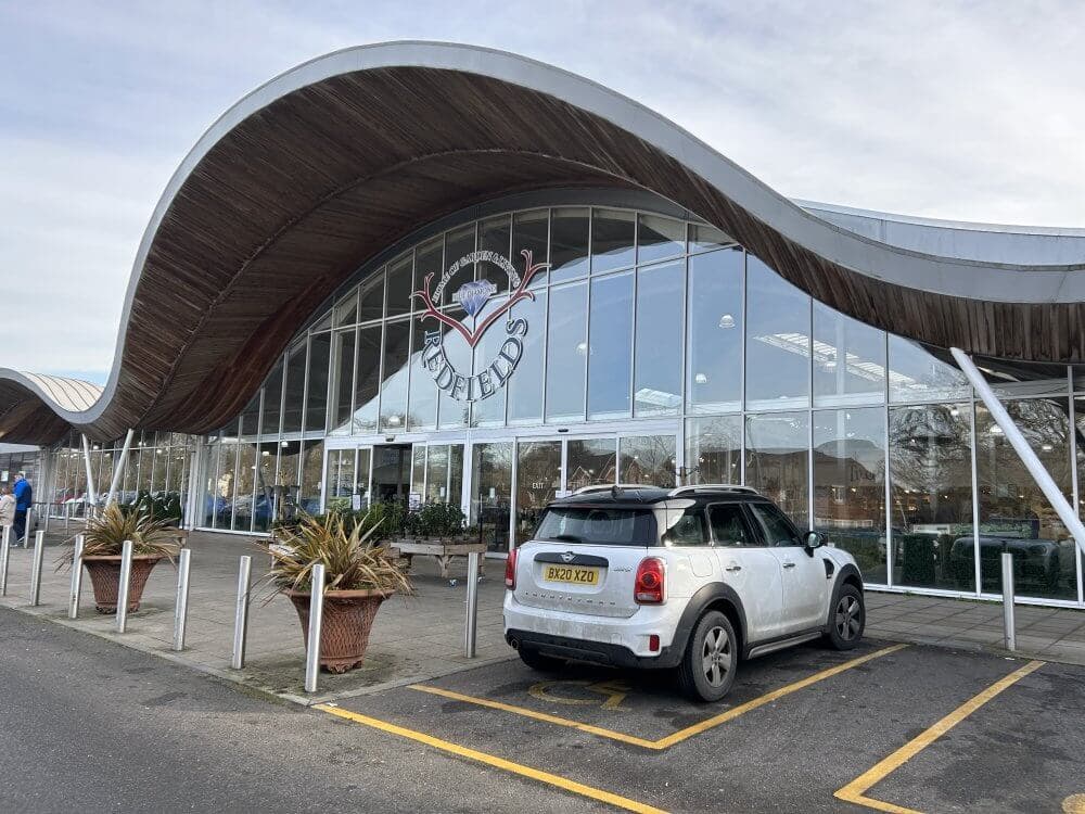 Home Instead Basingstoke picture of Redfields Garden Centre, Church Crookham, showing a white car parked in front of their modern, wavy-roofed entrance with large glass windows