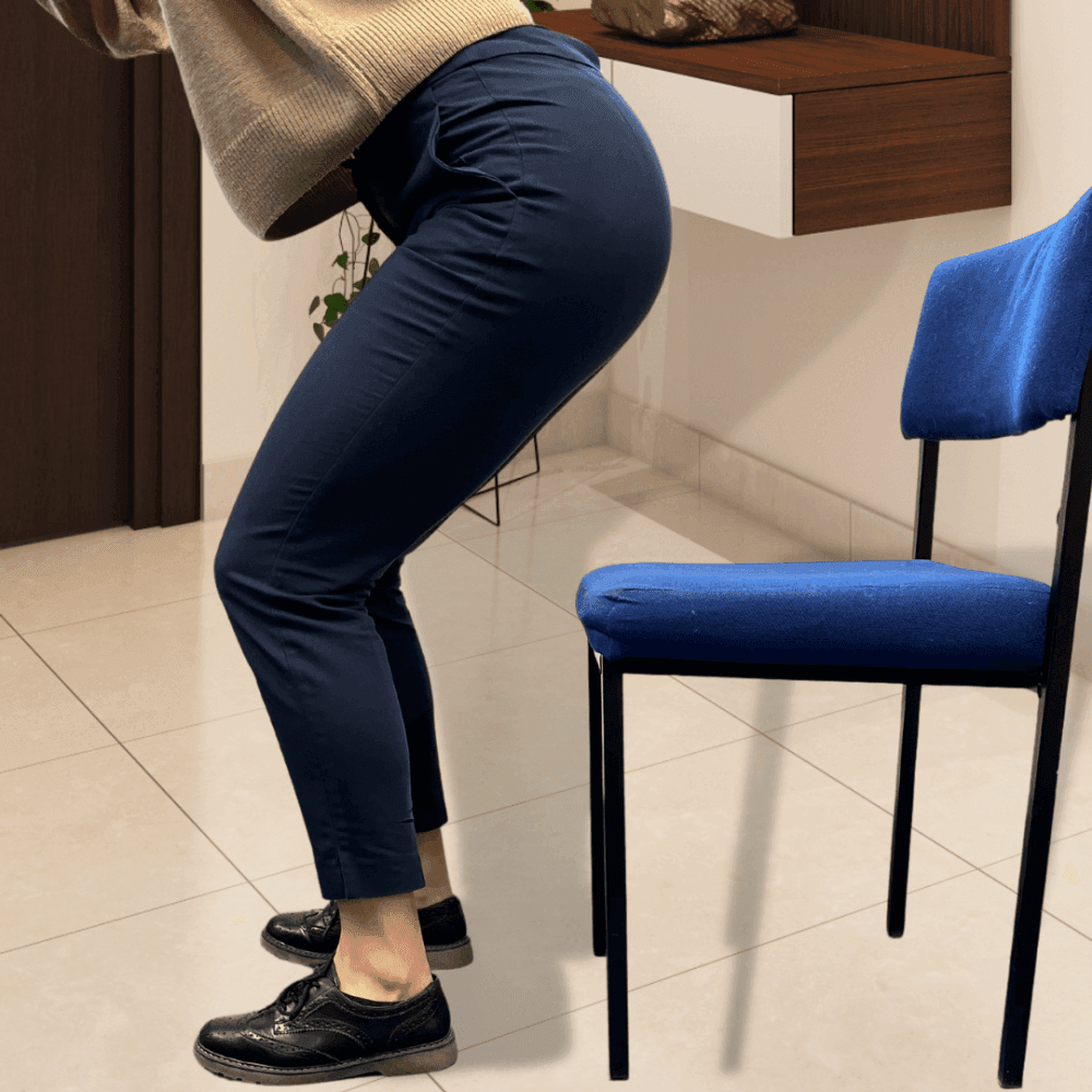Person in beige sweater and blue pants squats in front of a blue chair on a tiled floor. - Home Instead
