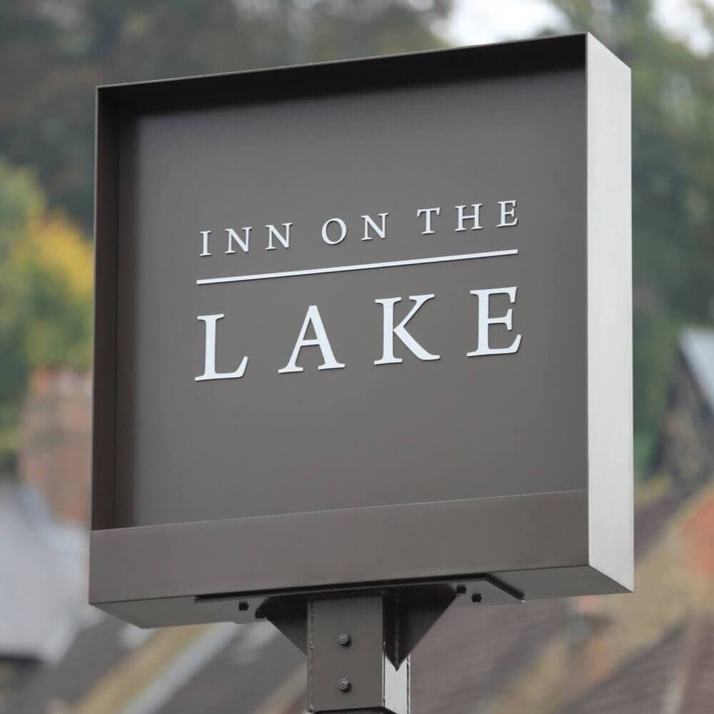 A sign reads "Inn on the Lake" with a blurred background of trees and buildings. - Home Instead