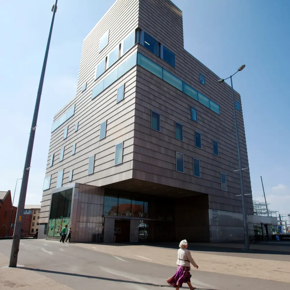 A modern multi-story building with a patterned facade, and a person walking by on a sunny day. - Home Instead