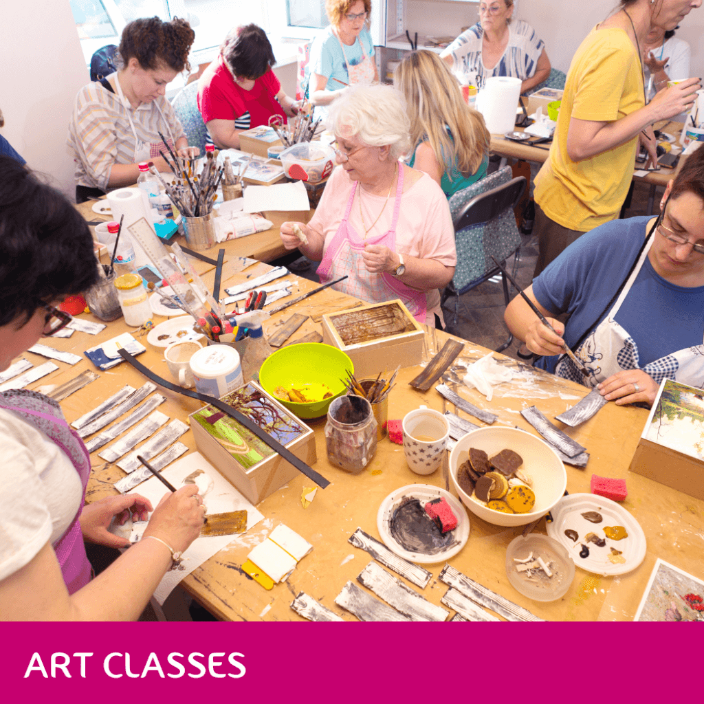 People of various ages engaged in an art class, painting and crafting. Sign at bottom says "Art Classes". - Home Instead