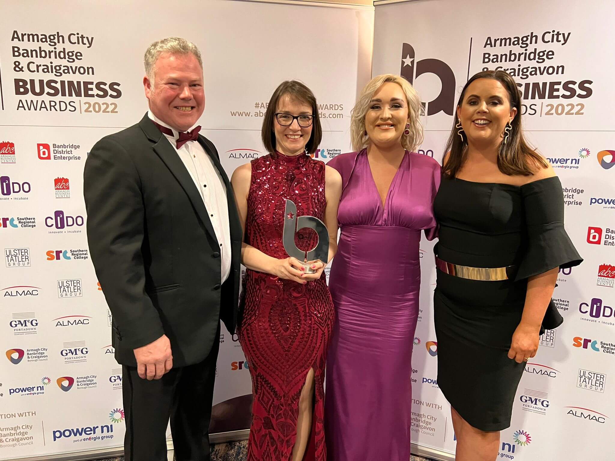 Four people dressed formally, smiling, and holding a trophy at the Armagh City, Banbridge & Craigavon Business Awards 2022. - Home Instead