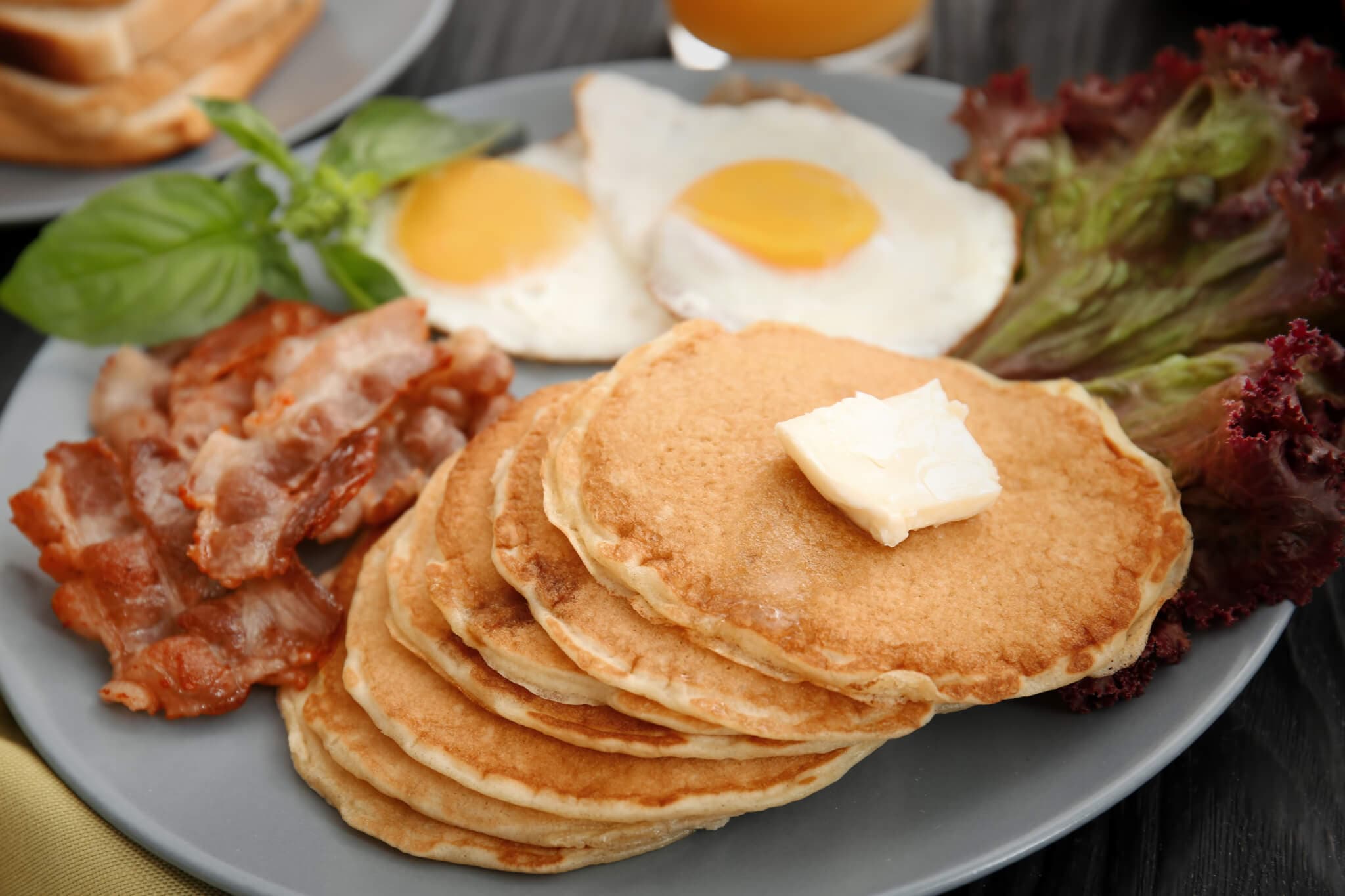 A plate with pancakes topped with butter, bacon strips, two sunny side up eggs, and lettuce garnish. - Home Instead