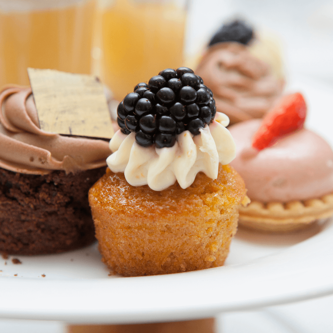 A plate of assorted desserts including a cupcake topped with a blackberry and a chocolate treat with a square garnish. - Home Instead