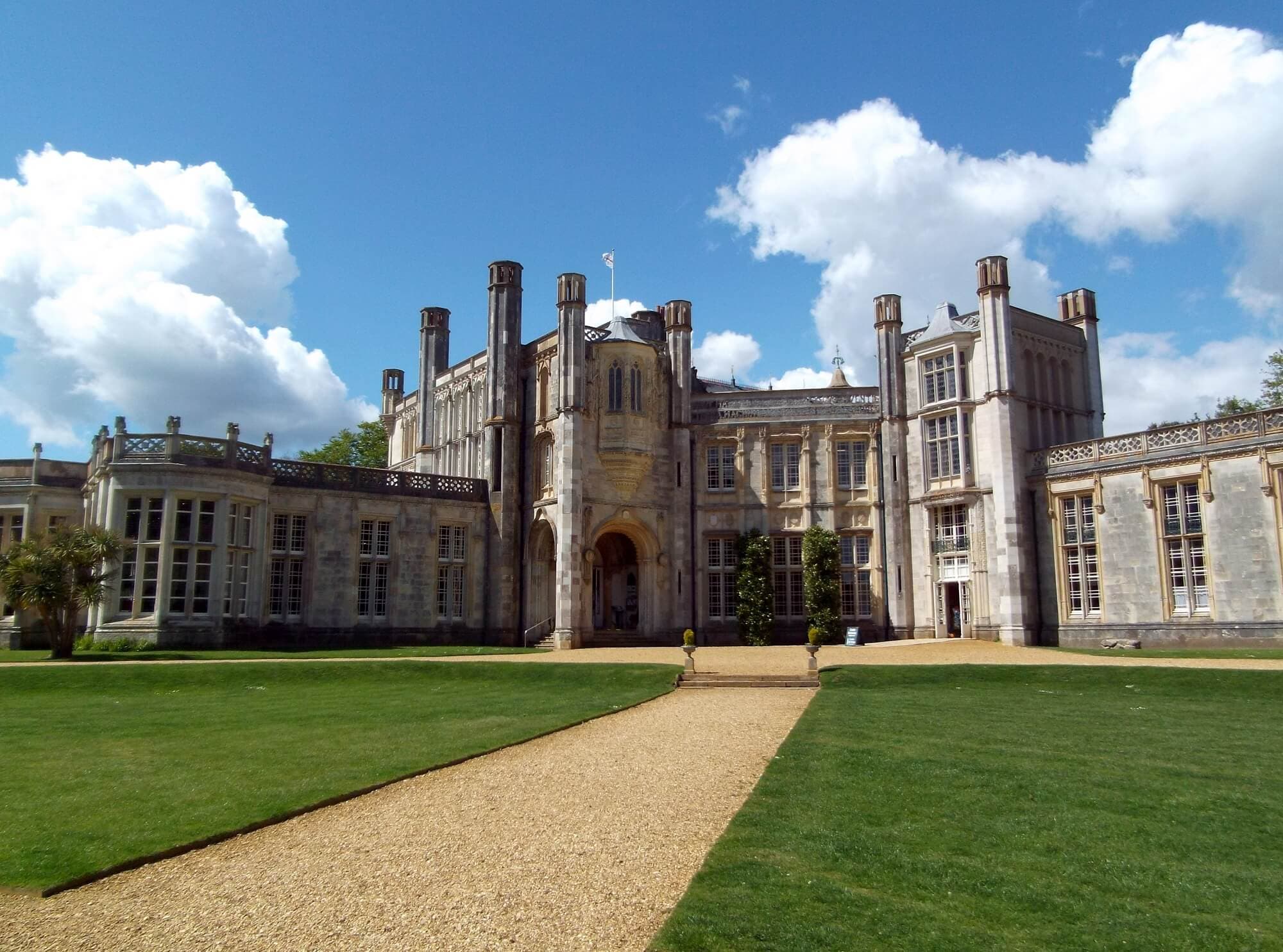 A grand historic mansion with a manicured lawn and a gravel path leading to its entrance under a bright blue sky. - Home Instead