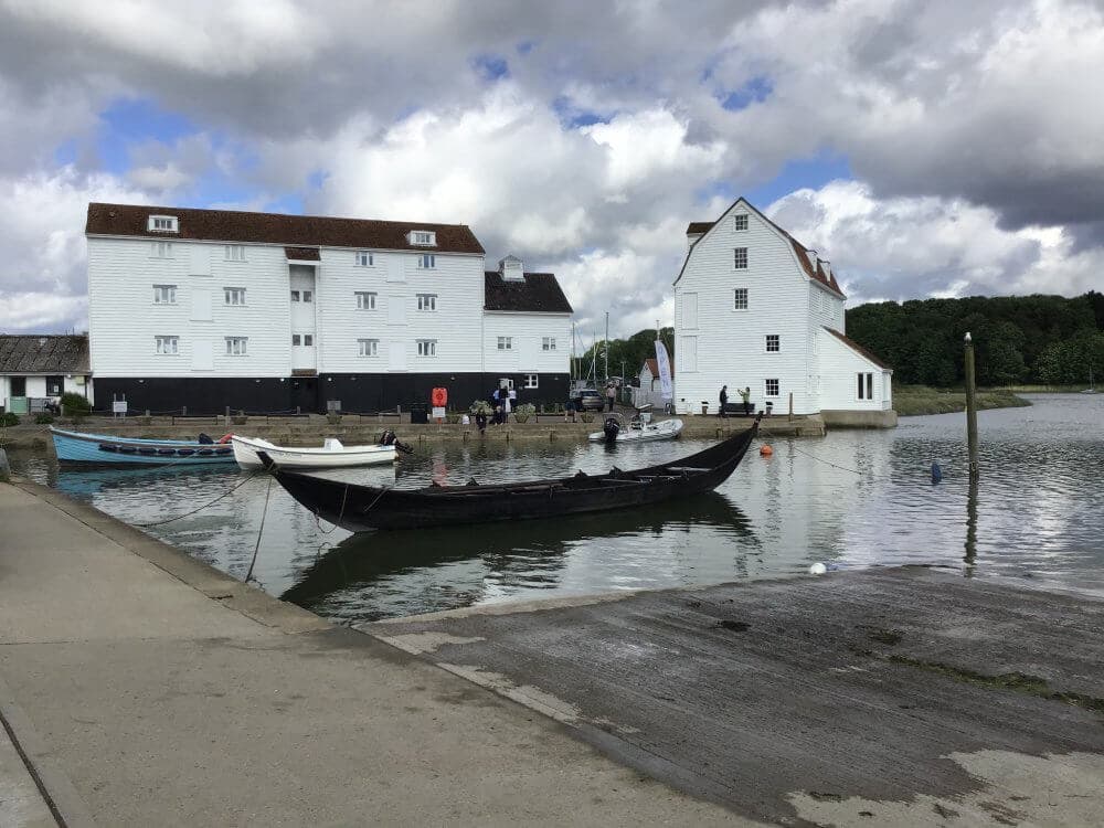 Small harbor with white buildings, boats docked on calm water, and a cloudy sky above. - Home Instead