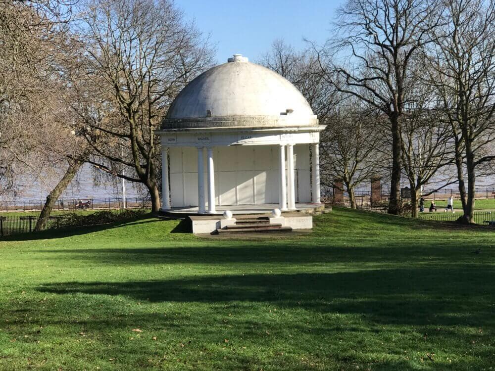 A white domed pavilion with columns stands on a lush green lawn surrounded by bare trees on a sunny day. - Home Instead