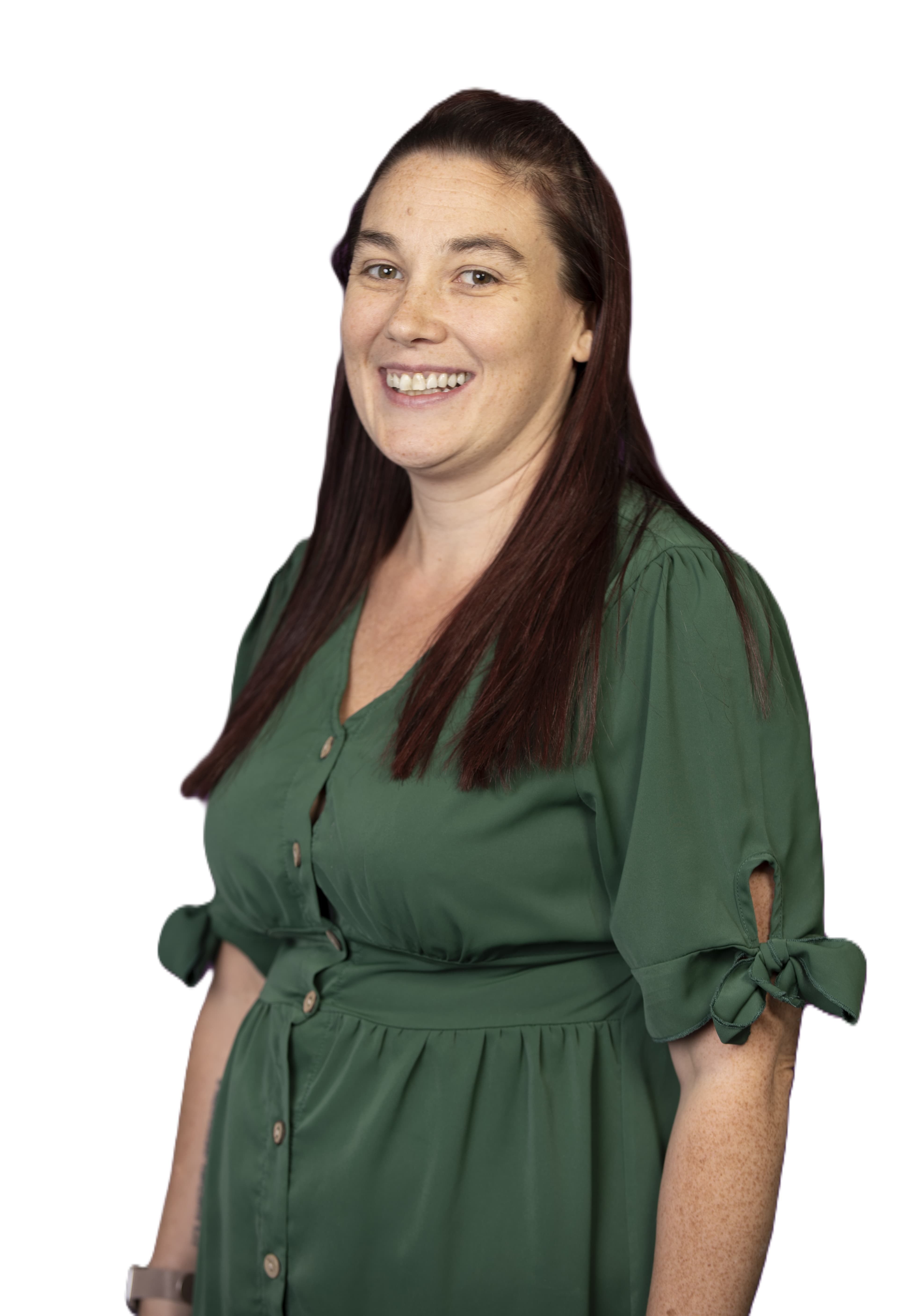 Woman with long brown hair in a green dress smiling, standing against a white background. - Home Instead