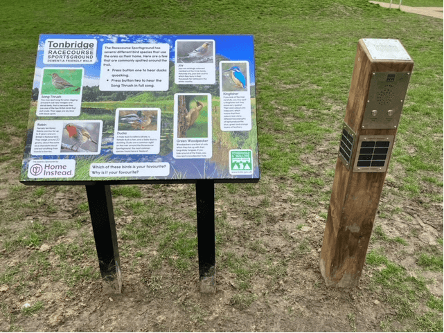 Informational sign and interactive bird panel at Tonbridge Racecourse Sports Ground on a muddy pathway. - Home Instead