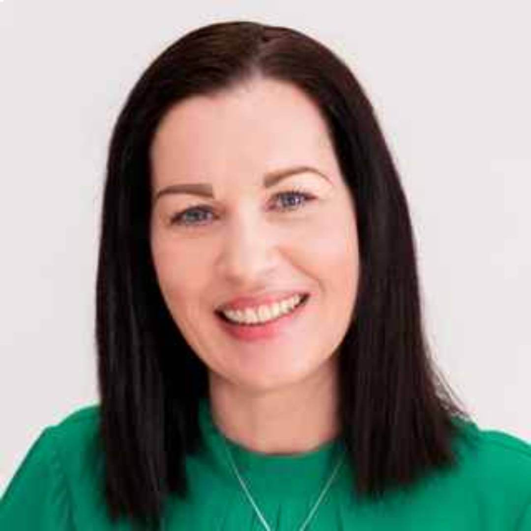 Woman with straight, long dark hair smiling, wearing a green top against a plain light background. - Home Instead