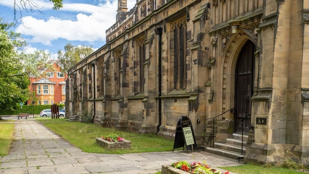 Historic stone church with gothic architecture, a small sign by the entrance reads "Open", and lawns with flower beds. - Home Instead