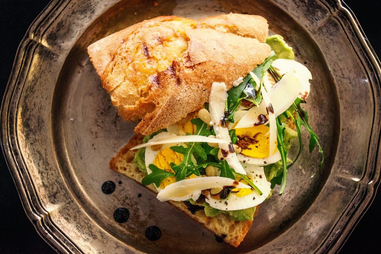 Sandwich with sliced hard-boiled eggs, arugula, and herbs on a rustic plate. - Home Instead