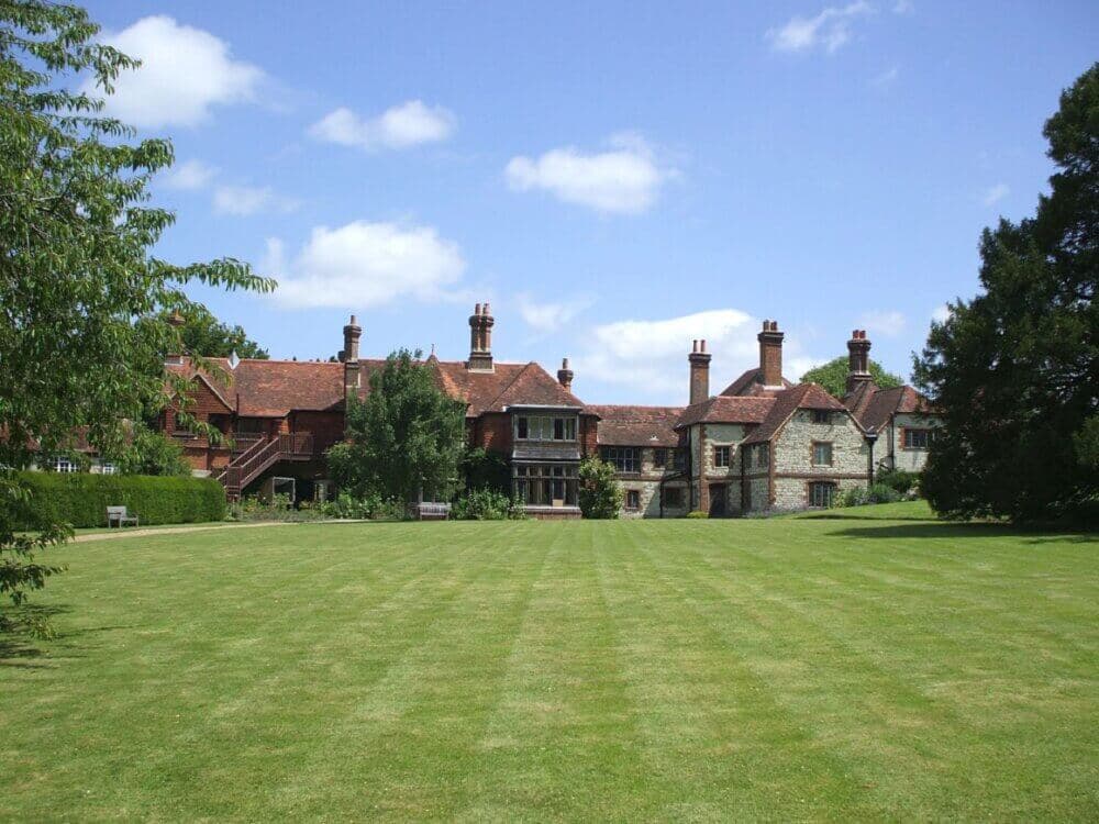 A large, historic brick building with multiple chimneys and a well-maintained lawn under a clear blue sky. - Home Instead