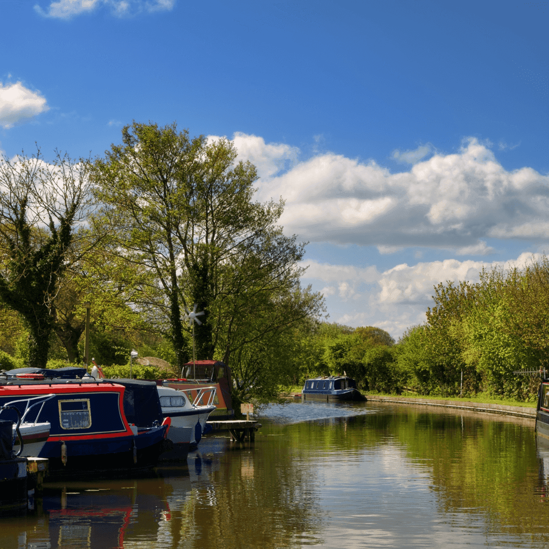 Canal with colorful narrowboats and trees on a bright, sunny day with a few clouds in the blue sky. - Home Instead