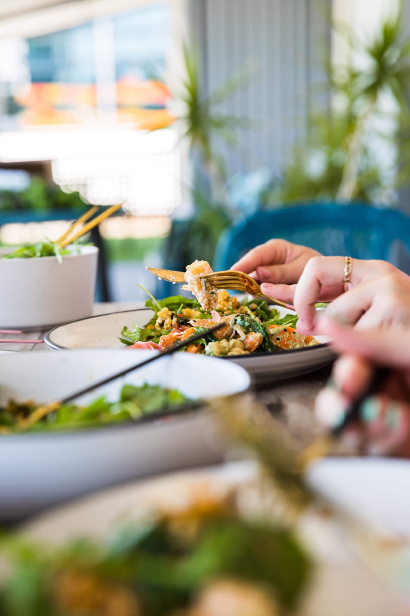 Close-up of people eating fresh salads with forks on a table outdoors. Green plants and bowls in the background. - Home Instead