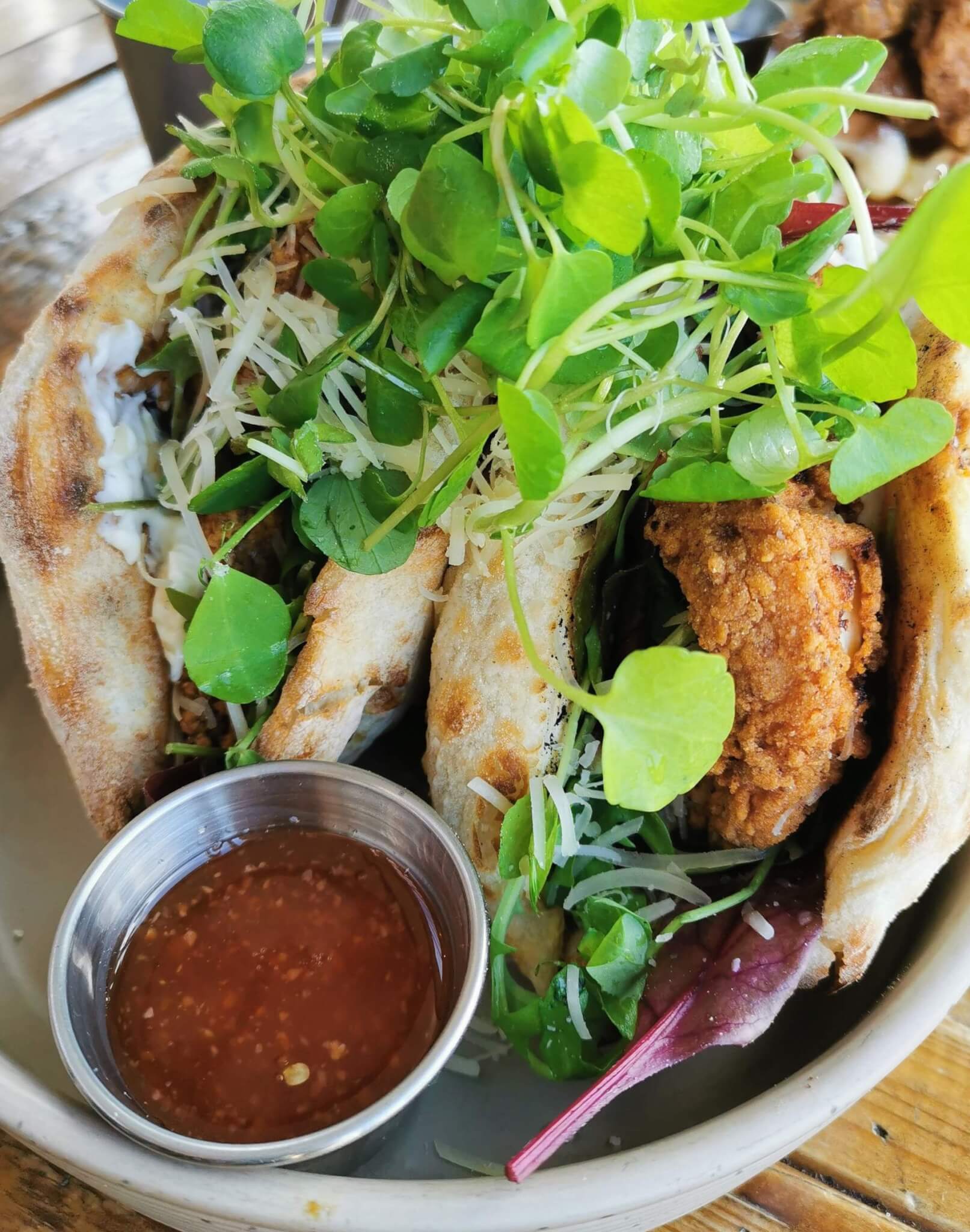 Close-up of a pita sandwich filled with fried chicken, greens, and sprouts, with a side of dipping sauce. - Home Instead