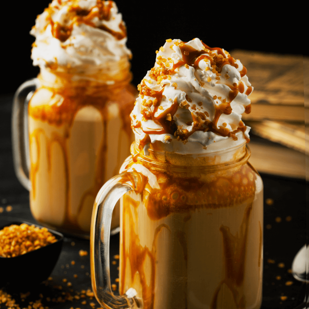 Two caramel milkshakes topped with whipped cream and caramel drizzle, served in mason jars against a dark background. - Home Instead