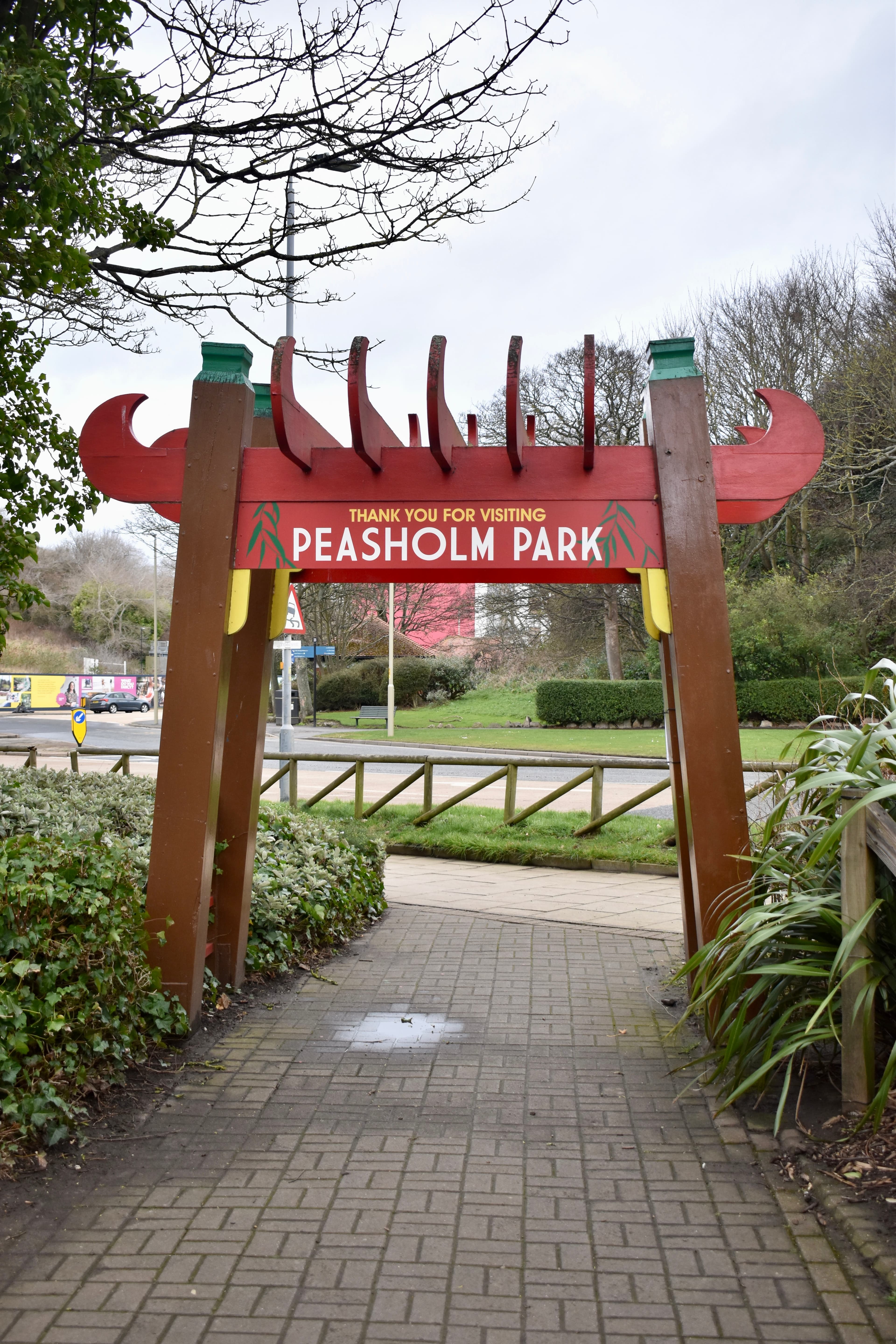 Entrance archway to Peasholm Park with a red sign and greenery around, viewed from the pathway leading inside. - Home Instead