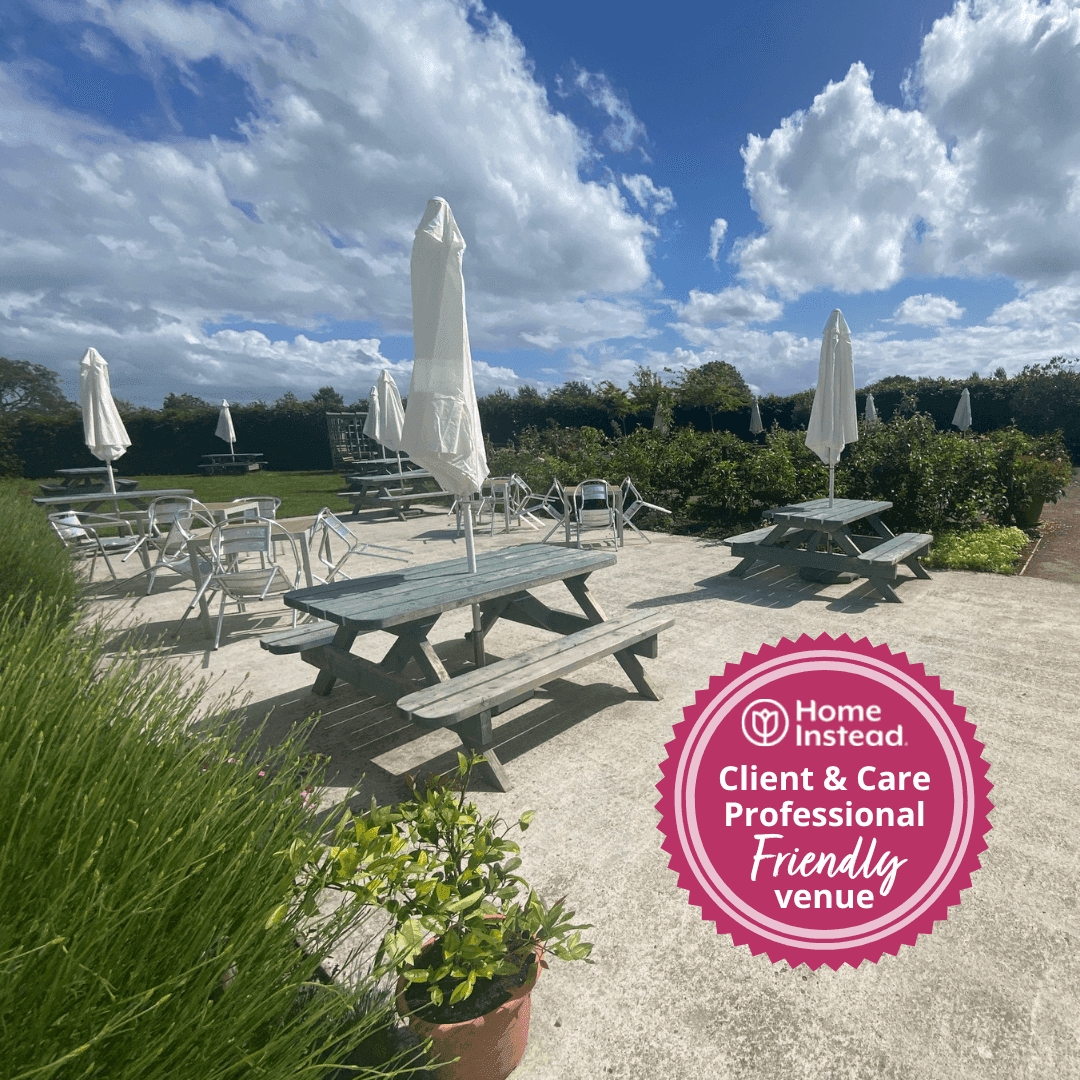 Outdoor area with picnic tables and umbrellas under a blue sky with clouds. "Home Instead Client & Care Professional Friendly venue. - Home Instead