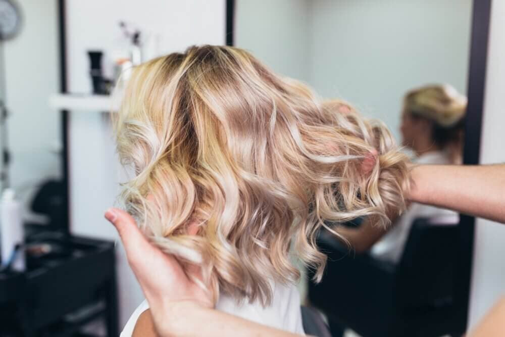 Hands styling a woman's wavy blonde hair in a salon. - Home Instead