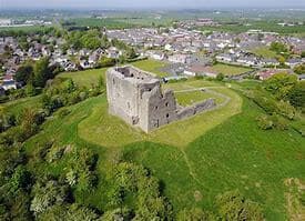Aerial view of the ruins of a stone castle on a grassy hill surrounded by a residential neighborhood. - Home Instead
