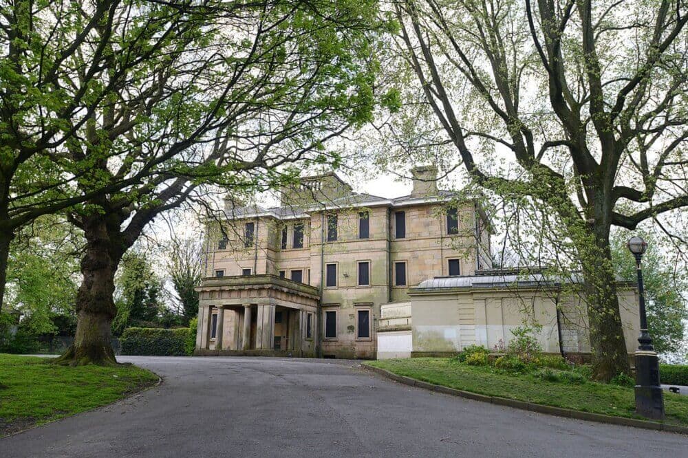 A large, elegant stone building surrounded by trees, with a driveway leading up to the entrance. - Home Instead